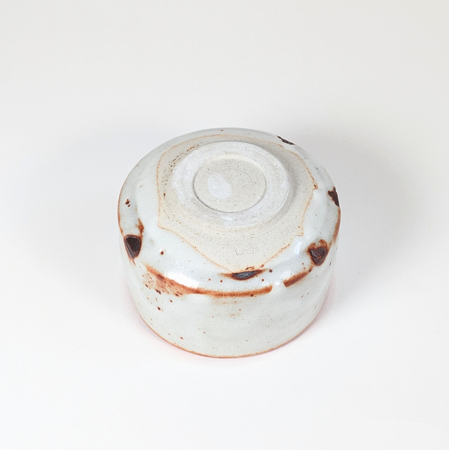 Vue complète du dessous du chawan Beni Shino, pied annulaire tourné, signature Keizan 桂山 et glaçure Shino blanche avec marques brun rouille.