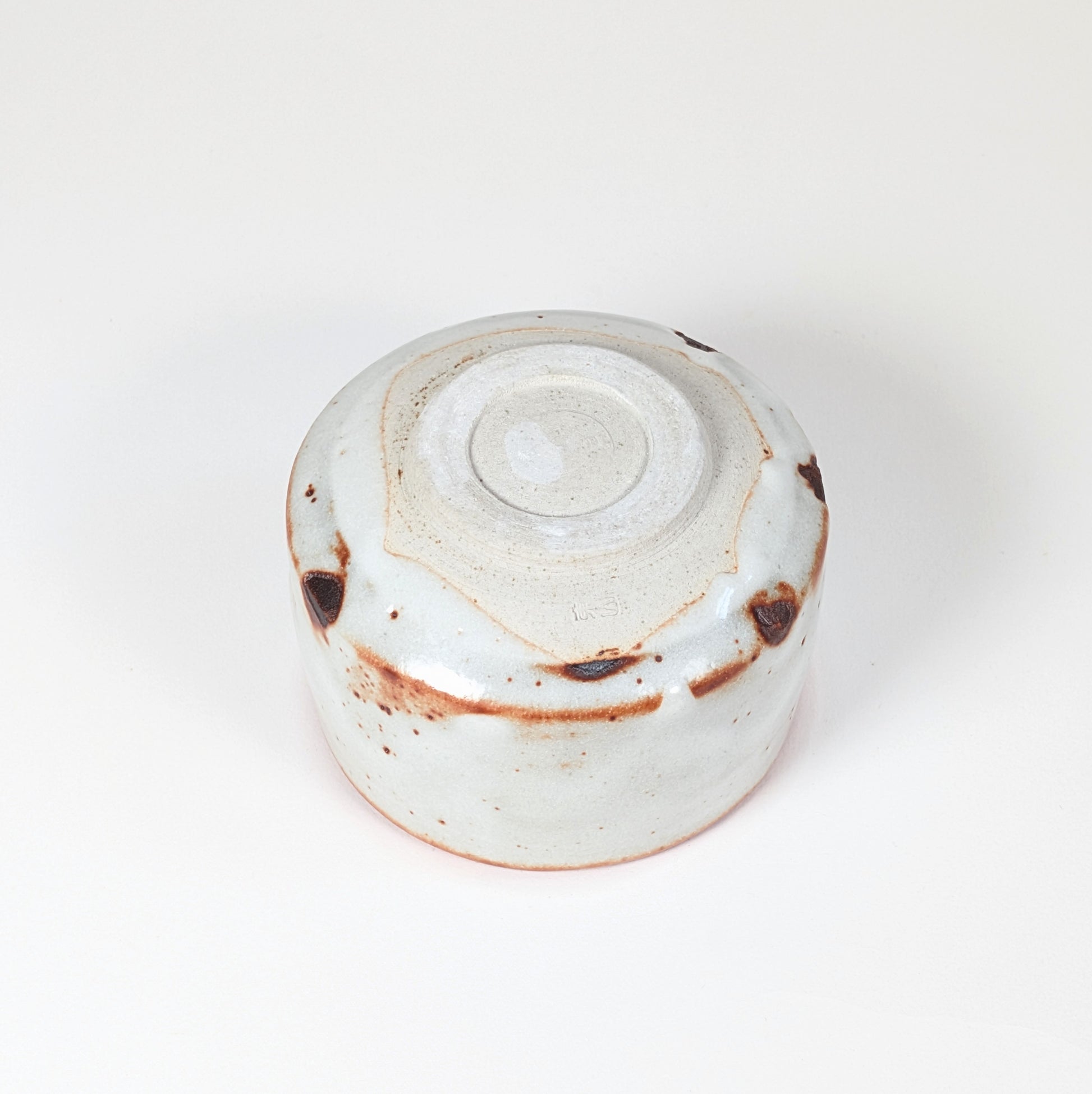 Vue complète du dessous du chawan Beni Shino, pied annulaire tourné, signature Keizan 桂山 et glaçure Shino blanche avec marques brun rouille.