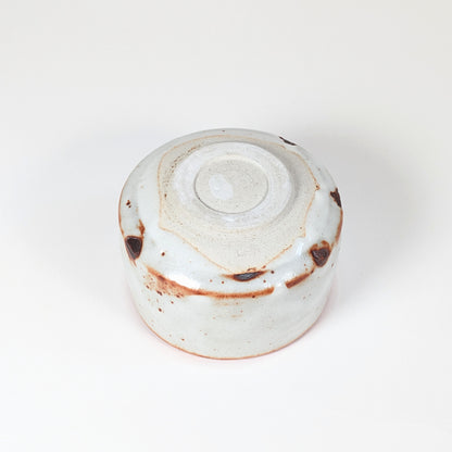 Vue complète du dessous du chawan Beni Shino, pied annulaire tourné, signature Keizan 桂山 et glaçure Shino blanche avec marques brun rouille.