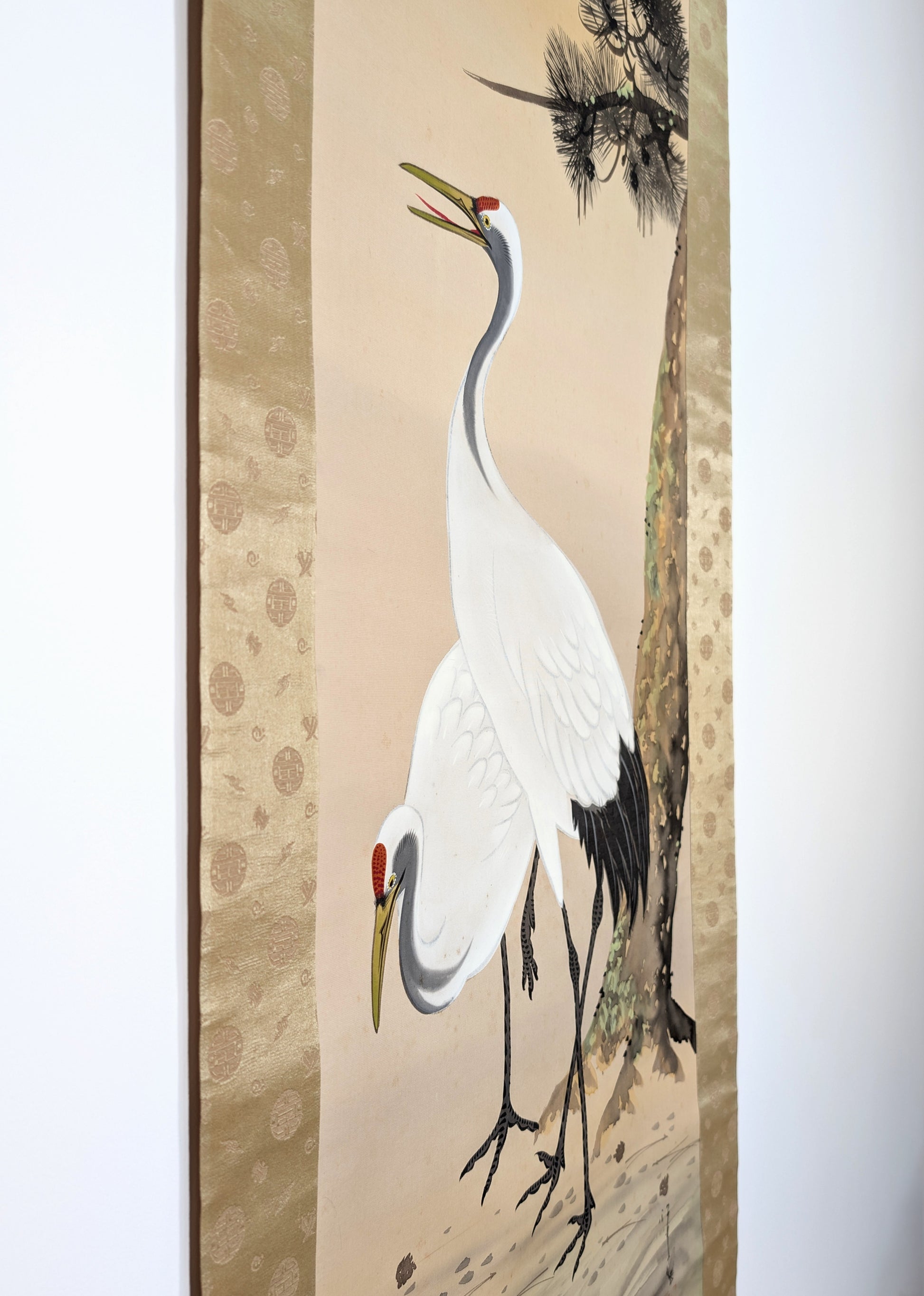 Vue de trois quarts du honshi peint sur soie avec les deux grues et le pin dans le montage traditionnel hyōsō.