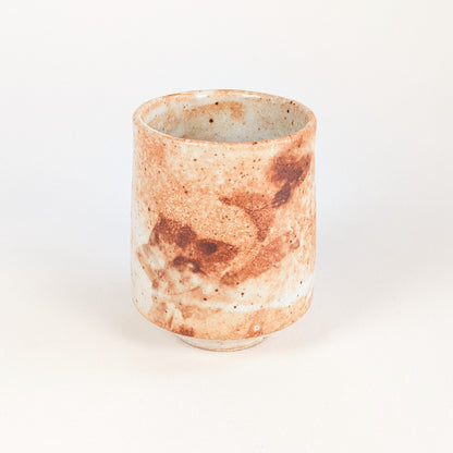 Tasse yunomi japonaise en céramique Shino, forme cylindrique et grandes taches brun rouille sur fond ivoire orangé.